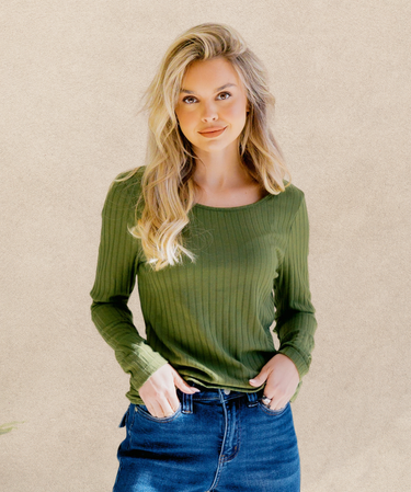 Woman wearing a green ribbed sweater and blue jeans against a beige background | Three Mad Hatters Mercantile